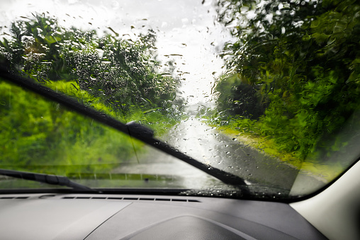 Driving in low visibility on the country road caused by the heavy rain, view from the car inside, focus on the rain drops on the windshield while the wipers are working