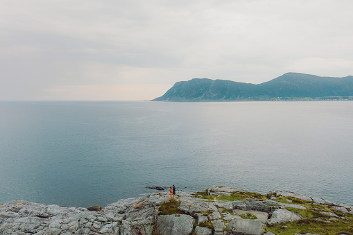 Drone photo of the couple with dog walking on the cliff contemplating a view of the sea and the green mountain peaks in More og Romsdal, Norway