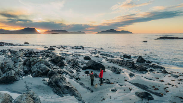 Aerial view of woman and man having picnic at the beach admiring sunset  with scenic view in Norway stock photo