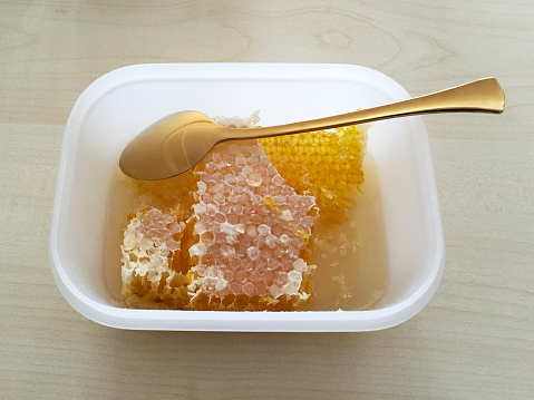 close-up of honey container with clamp taking out a piece of honeycomb from inside.