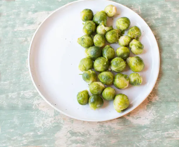 Fresh cooked brussels sprouts served for side dish on a half full plate isolated on green, wooden table background from above with copy space