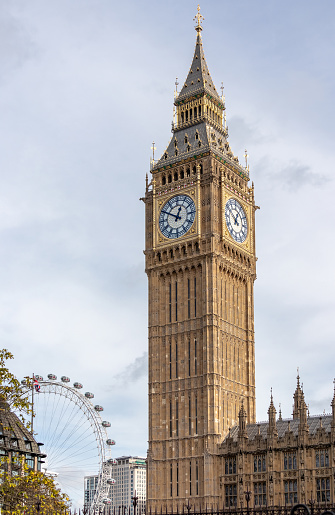 La torre del reloj del palacio de Westminster, comúnmente conocida bajo el nombre de su campana - Big Ben - ubicada en Londres, Reino Unido. El London Eye, otro hito bien conocido es visible en el fondo. photo