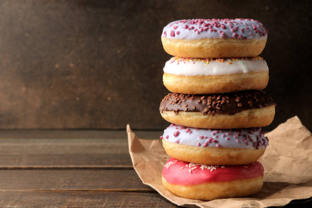 istock Assorted sweet donuts stacked on a brown wooden table with icing and sprinkling. with space for text 1440531649