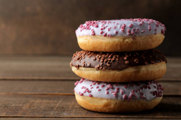 istock Assorted sweet donuts stacked on a brown wooden table with icing and sprinkling. 1440531712