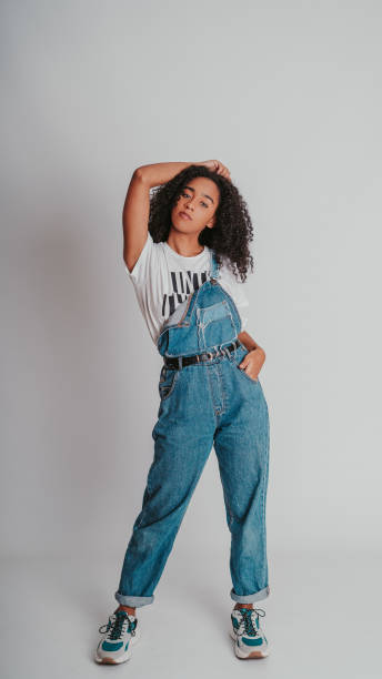 portrait of a curly hispanic female wearing denim overalls and posing against a wall - 工人褲 個照片及圖片檔