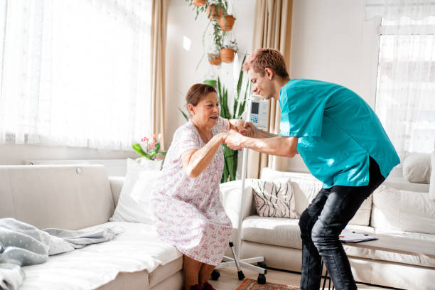 медицинский работник помогает пожилым женщинам встать в гостиной - residential care фотографии стоковые фото и изображения