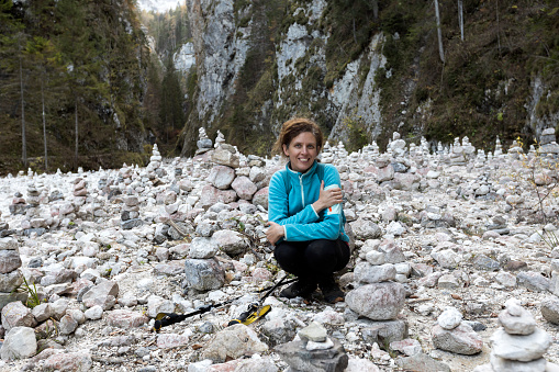 Serene Mid Adult Woman Hiker Happy on a Hike trough a Valley of Stack Stone Towers by Hikers - Martuljek Waterfalls Hiking Travel Destination