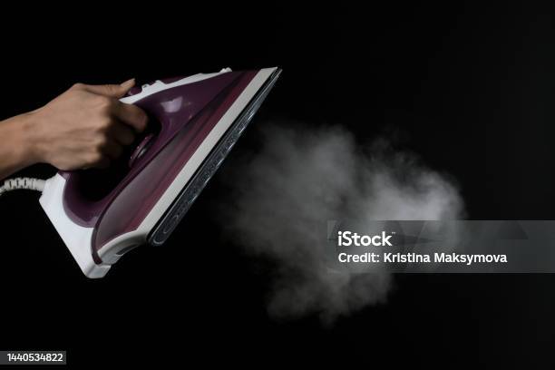 The Girl Lets Out Steam From The Lilac Iron On A Black Background Ironing Clothes Household Electrical Appliances Stock Photo - Download Image Now