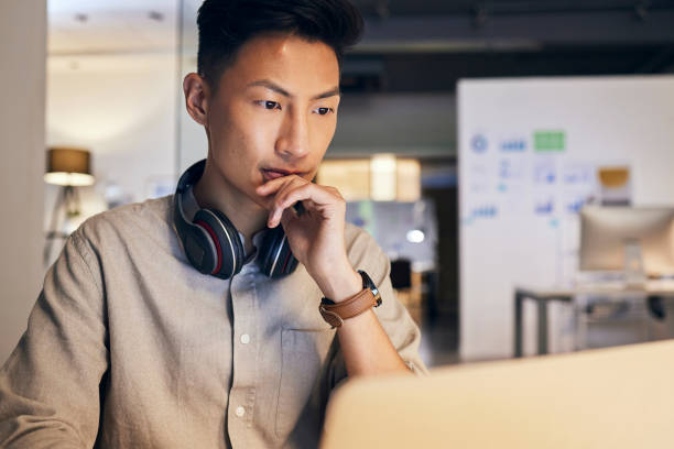 istock Thinking, laptop and it business man in office for website design, software development or market research work with headphones. Information technology, computer and asian man for digital analytics 1440535144