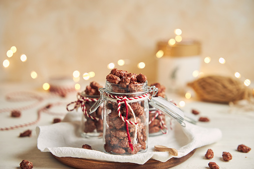 The Delicious Christmas roasted almonds in a jar on a wooden plate and a white table