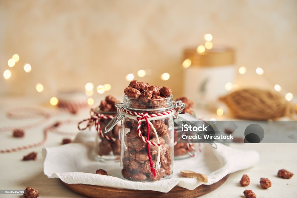Delicious Christmas roasted almonds in a jar on a wooden plate and a white table The Delicious Christmas roasted almonds in a jar on a wooden plate and a white table Holiday - Event Stock Photo