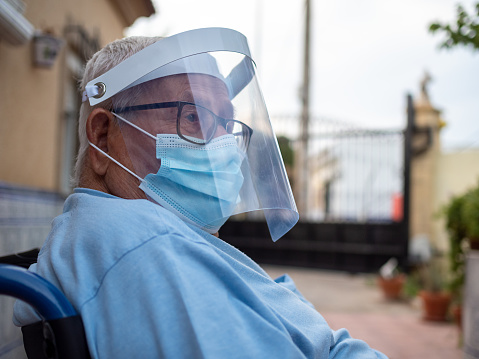 Senior man in a wheelchair wearing a face shield and a mask - Coronavirus/Covid-19 concept