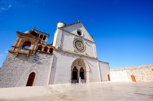 The beautiful and harmonious facade of the Basilica Superiore di San Francesco (Upper Basilica of St Francis) in the medieval town of Assisi, in Umbria. Built in the Italian Gothic style starting from 1228 and completed in 1253, the Basilica, which preserves the mortal remains of the Saint of the Poor from 1230, is composed of the Basilica Inferiore (Lower Basilica) and the Basilica Superiore (Upper Basilica), perfectly integrated. Over the centuries Assisi and the spirituality of its sacred places have become a symbol of peace, a point of reference for tolerance and solidarity between peoples and between the different confessions of the world. The Umbria region, considered the green lung of Italy for its wooded mountains, is characterized by a perfect integration between nature and the presence of man, in a context of environmental sustainability and healthy life. In addition to its immense artistic and historical heritage, Umbria is famous for its food and wine production and for the high quality of the olive oil produced in these lands. Since 2000 the Basilica and other Franciscan sites of Assisi have been declared a World Heritage Site by UNESCO. Super wide angle image in high definition format.