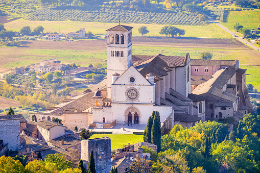 A splendid landscape of the green Umbria Valley with in the foreground the Basilica Superiore di San Francesco (Upper Basilica of St Francis), the Sacro Convento (the Franciscan Monastery) and a glimpse of the medieval town of Assisi. Built in the Italian Gothic style starting from 1228 and completed in 1253, the Basilica, which preserves the mortal remains of the Saint of the Poor from 1230, is composed of the Basilica Inferiore (Lower Basilica) and the Basilica Superiore (Upper Basilica), perfectly integrated. Over the centuries Assisi and the spirituality of its sacred places have become a symbol of peace, a point of reference for tolerance and solidarity between peoples and between the different confessions of the world. The Umbria region, considered the green lung of Italy for its wooded mountains, is characterized by a perfect integration between nature and the presence of man, in a context of environmental sustainability and healthy life. In addition to its immense artistic and historical heritage, Umbria is famous for its food and wine production and for the high quality of the olive oil produced in these lands. Since 2000 the Basilica and other Franciscan sites of Assisi have been declared a World Heritage Site by UNESCO. Image in high definition format.