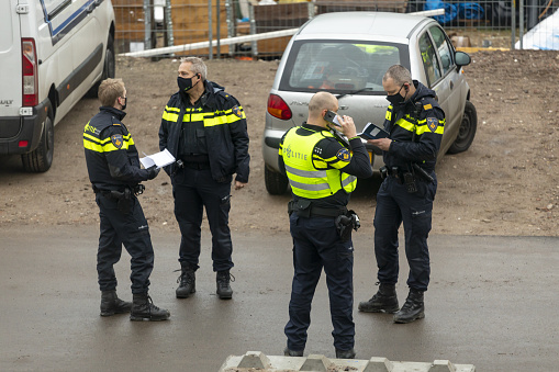 Zutphen, Netherlands – December 08, 2020: Police officers in face masks deliberating and organizing at an accident scene with notebooks and cellphone in hand