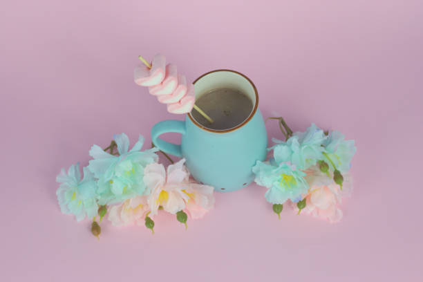 istock Blue ceramic mug with hot chocolate and marshmallows on a stick, with flowers on a pink background 1440537518