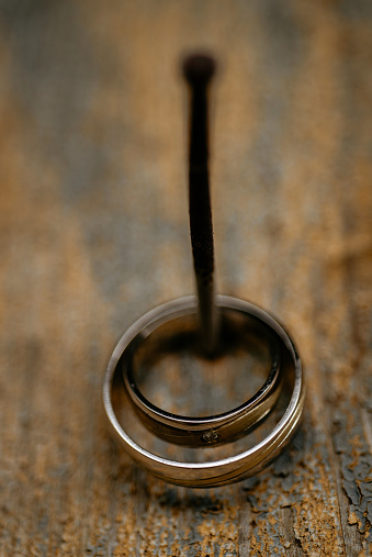 A vertical shot of silver wedding rings hanging on a nail against a wooden wall