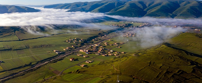 An aerial of the clouds over the small town surrounded by mountains.