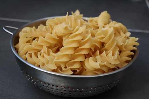 A closeup of the raw fresh fusilli pasta in a steel colander on a gray surface