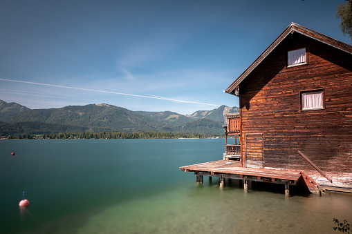 A small wooden house on a lake with long exposure surrounded by hills in Hallsatt, Austria