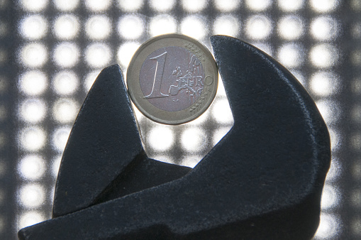 A spanner holding a euro coin on led lights background - the concept of limited finances