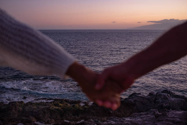 ぼやけた女性と男性の手がビーチでお互いを抱きしめている。海の夕焼けの光の上の地平線 - trust human hand sea of hands holding ストックフォトと画像