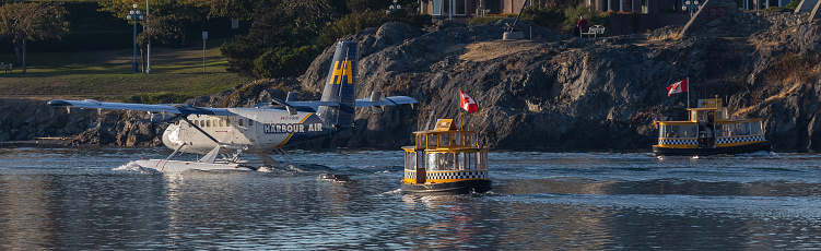 Victoria, Canada – September 05, 2018: Victoria, BC, Canada - September 4, 2018: Yellow water taxis and water plane sailing at sunset in the harbor with passengers inside.