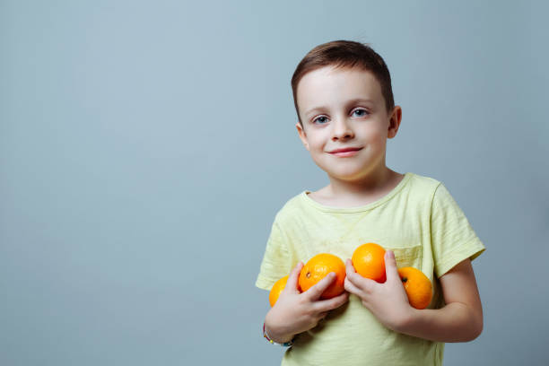 child with tangerines in his hands smiling softly against a uniform background. stock photo