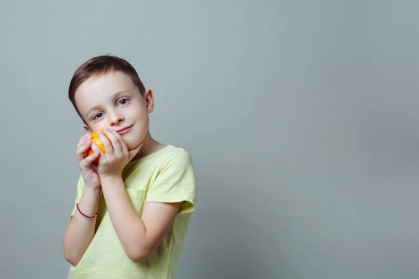child with tangerine in his hands smiling softly and gently presses it to the face stock photo