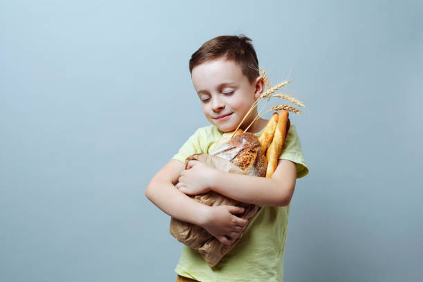small child lovingly embraces a bag of groceries with freshly baked bread, smiling softly, holding the bread tightly to his chest. stock photo