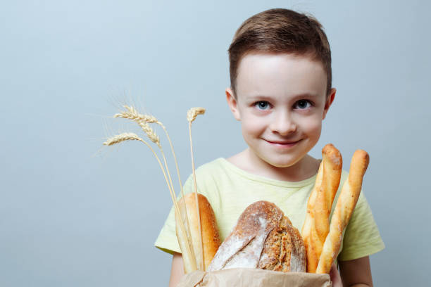 child with a grocery bag with freshly baked bread and ears of wheat, smiling softly. close up stock photo