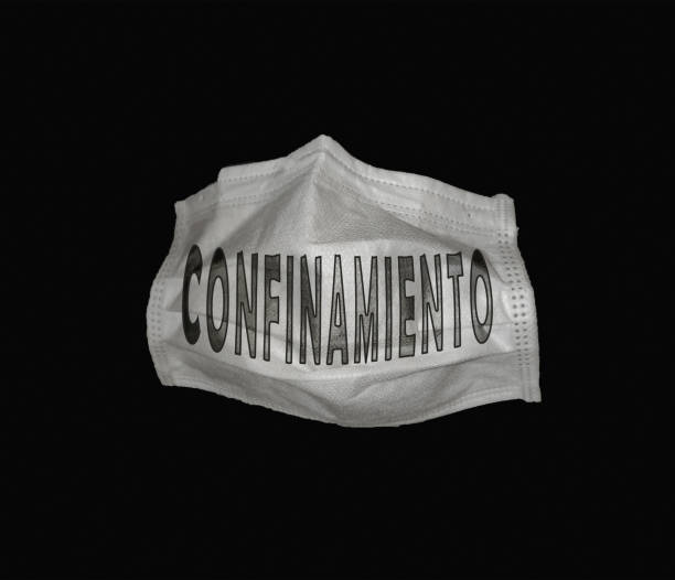 Closeup of a facemask with "confinamiento - lockdown" written on it isolated on a black background A closeup of a facemask with "confinamiento - lockdown" written on it isolated on a black background confinamiento stock pictures, royalty-free photos & images