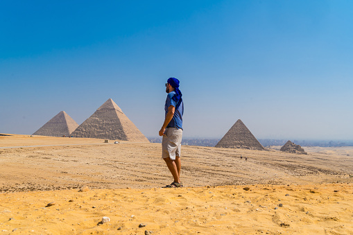 A portrait of a young man in a blue turban walking next to the Pyramids of Giza, Cairo, Egypt