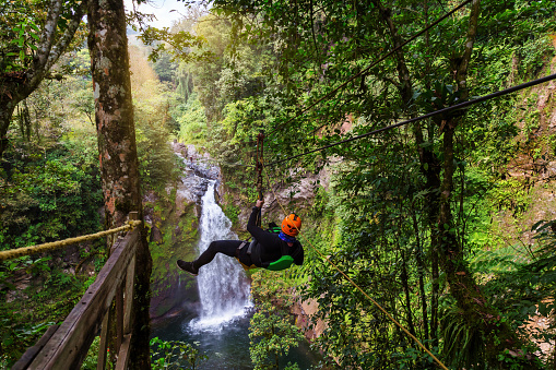 Young man riding on a zip line rope in an extreme adventure jungle in XiVeracruz, Mexico