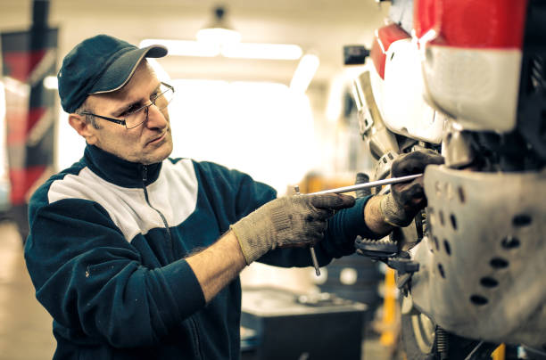 europäischer mechaniker mit brille bei der arbeit an einem motorrad in einer garage - mechanician stock-fotos und bilder