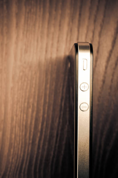 A vertical shot of a smartphone and its volume buttons on a wooden surface