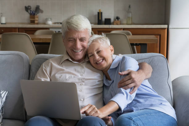 istock Happy older spouses relaxing on sofa at home using laptop 1440554602