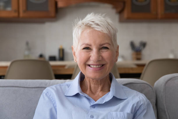 istock Older woman resting on sofa smiling staring at camera 1440554610