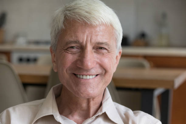 istock Happy older man sits indoors looking at camera 1440555065