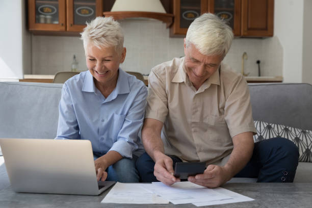 пожилые супруги, управляющие финансами, использующие ноутбук, оплачивающие счета через электронный банк - middle human age couple women стоковые фото и изображения
