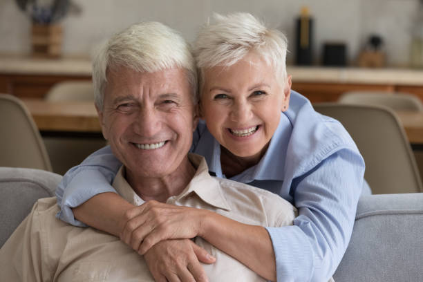 istock Loving wife hugs husband seated on sofa staring at camera 1440555157