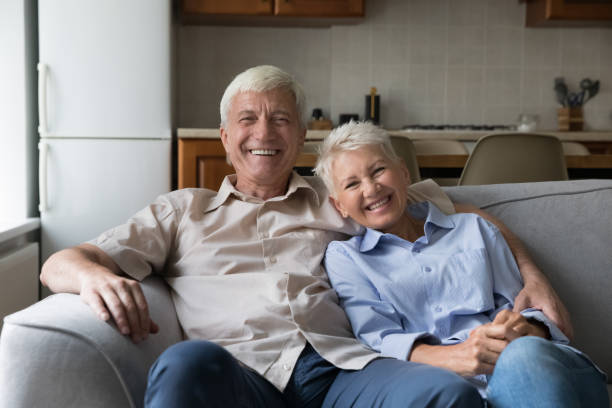 istock Older couple resting sit on couch laughing staring at camera 1440555158