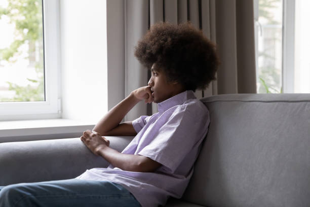istock Sad African teenage guy sits on sofa looking through window 1440555312