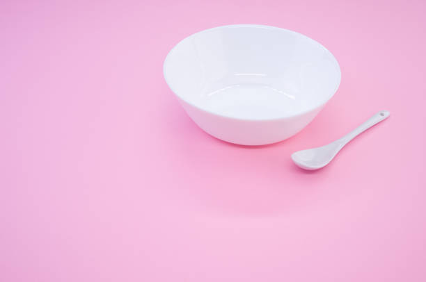 A high angle shot of a spoon placed on a white bowl on a pink background shot on a studio