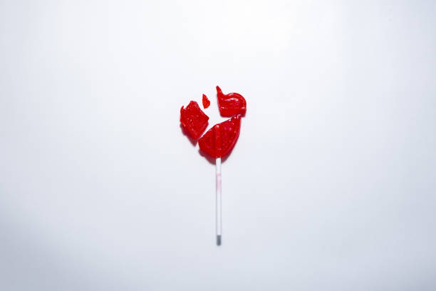 A heart-shaped lollipop broken into several pieces on a white table - heartbreak concept
