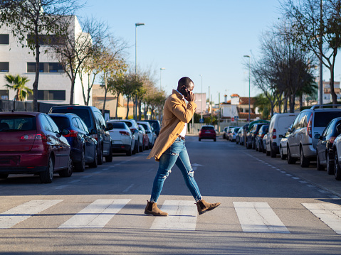 A shallow focus of a stylish African male talking on the phone while crossing the street