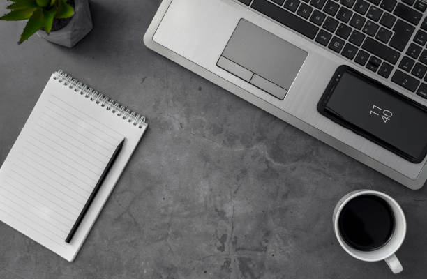 istock Top view grayscale shot of a laptop, mobile phone, coffee, and notebook on a table 1440559446