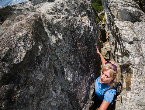 Blond female squeezes between the narrow cleft between sandstone rocks while exploring the summit atop Seneca Rocks, West Virginia. USA