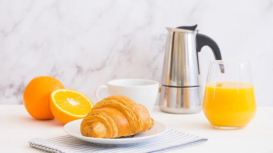 Breakfast laid on the table. Coffee, atelsin juice and croissant