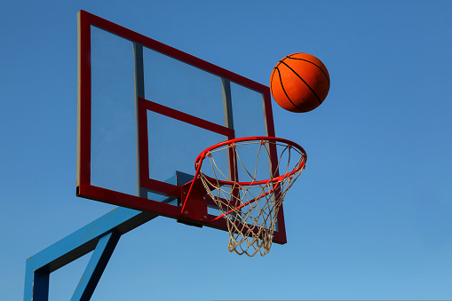 A basketball against the blue sky is flying into the basket. Outdoor basketball court.